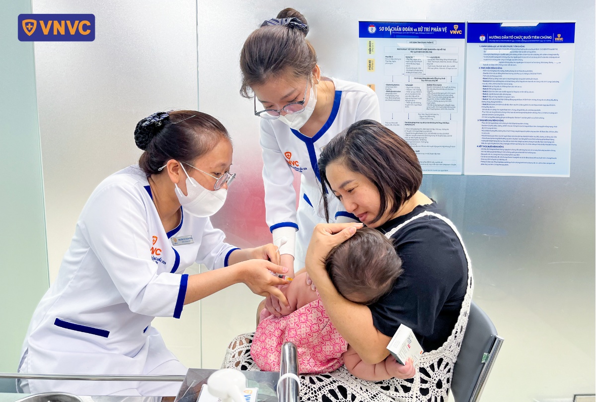 mẹ bế bé cho điều dưỡng tiêm phòng